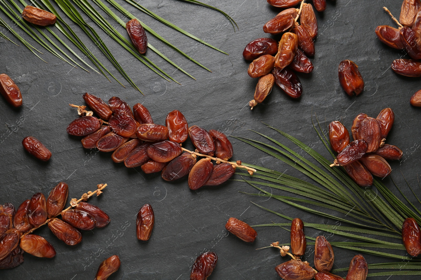 Photo of Tasty sweet dried dates and green leaves on black table, flat lay