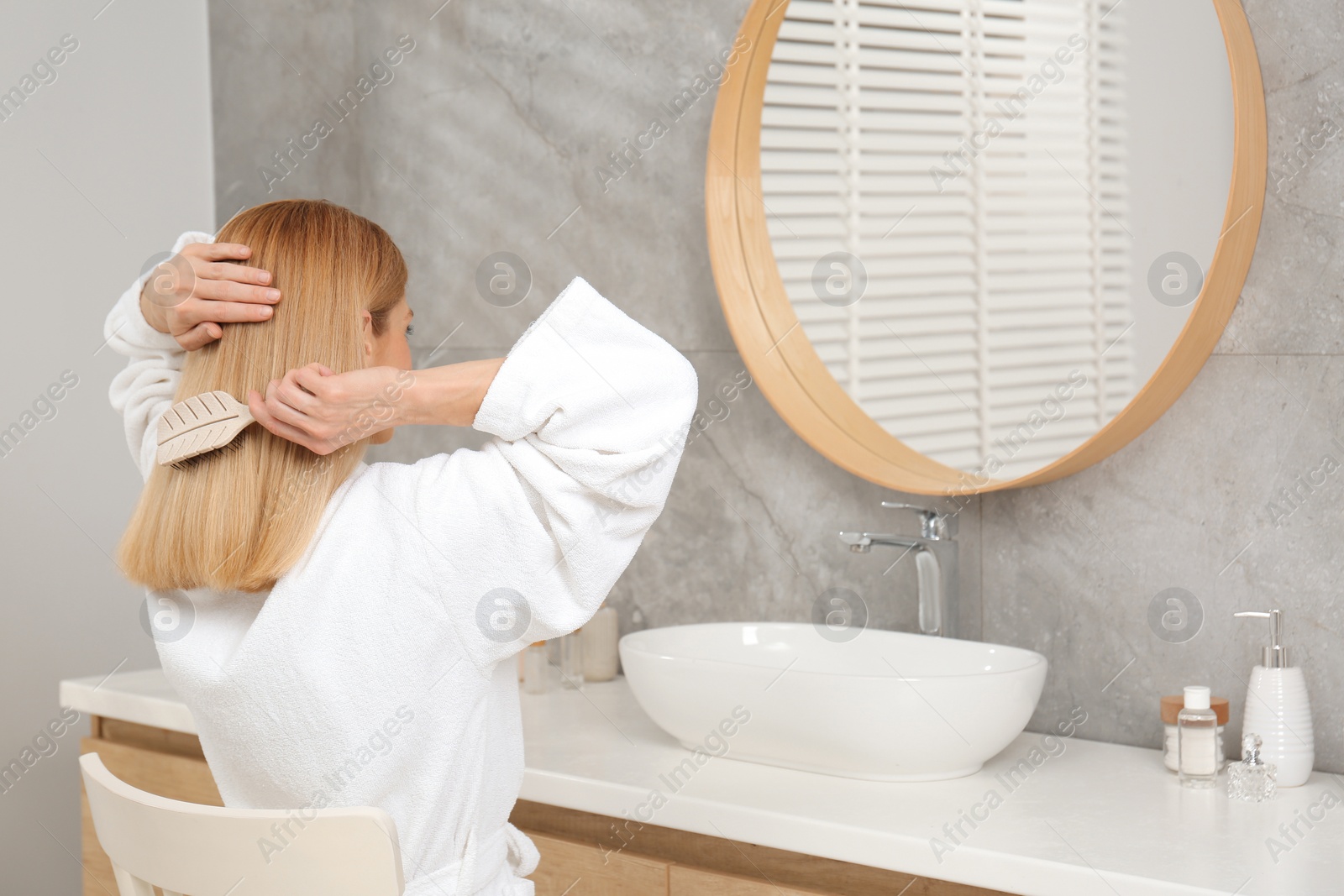 Photo of Beautiful woman brushing her hair near mirror in bathroom
