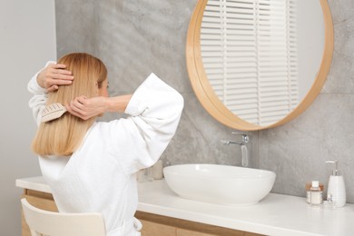 Photo of Beautiful woman brushing her hair near mirror in bathroom