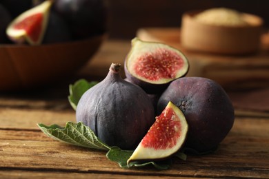 Photo of Whole and cut tasty fresh figs with green leaf on wooden table, closeup