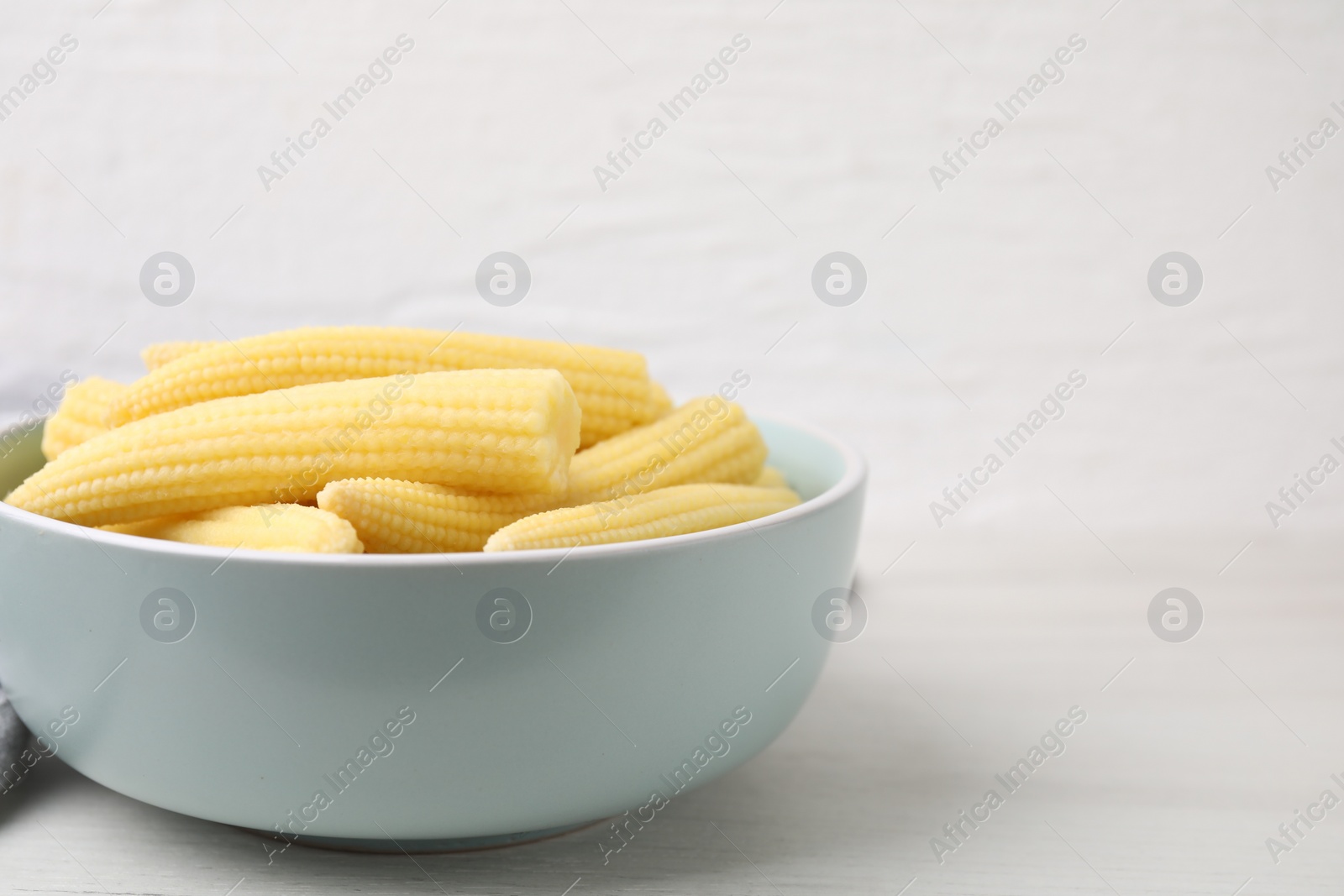 Photo of Tasty fresh yellow baby corns in bowl on white wooden table, closeup. Space for text