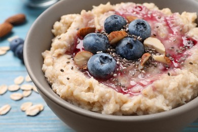 Photo of Tasty oatmeal porridge with toppings on light blue wooden table, closeup