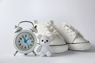 Alarm clock, toy bear and baby booties on white background. Time to give birth