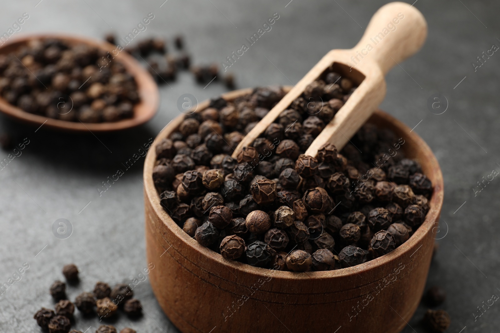 Photo of Aromatic spice. Pepper in bowl and scoop on black table, closeup