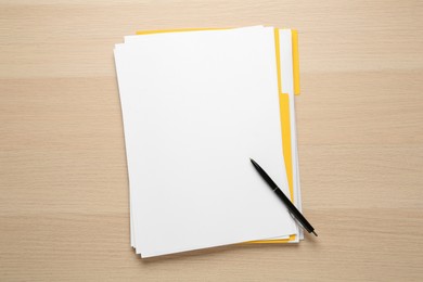 Photo of Yellow file with blank sheets of paper and pen on wooden table, top view. Space for design