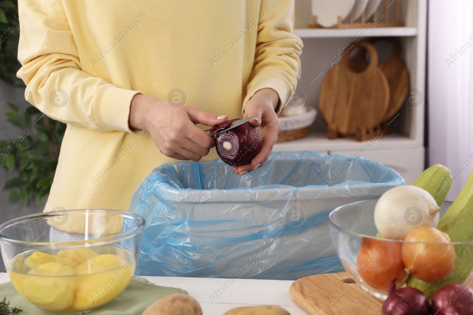 Photo of Woman peeling fresh onion with knife above garbage bin indoors, closeup