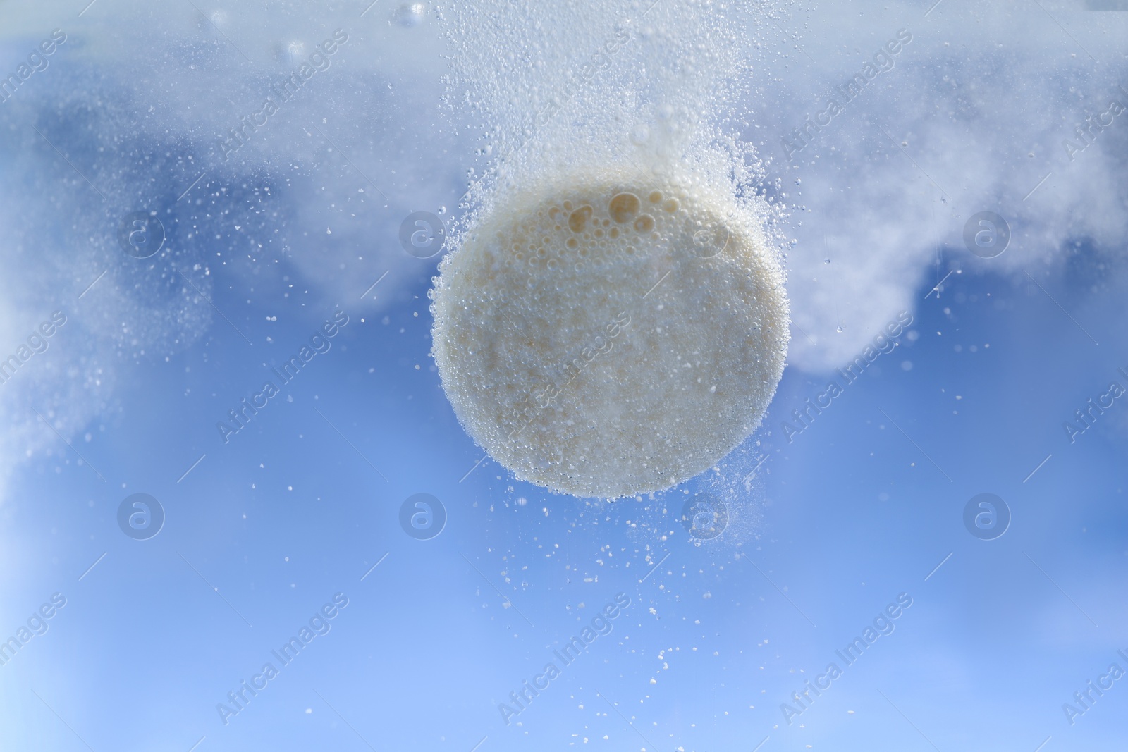 Photo of Effervescent pill dissolving in water on light blue background, closeup