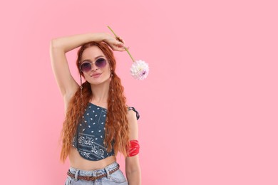 Stylish young hippie woman with dahlia flower on pink background, space for text
