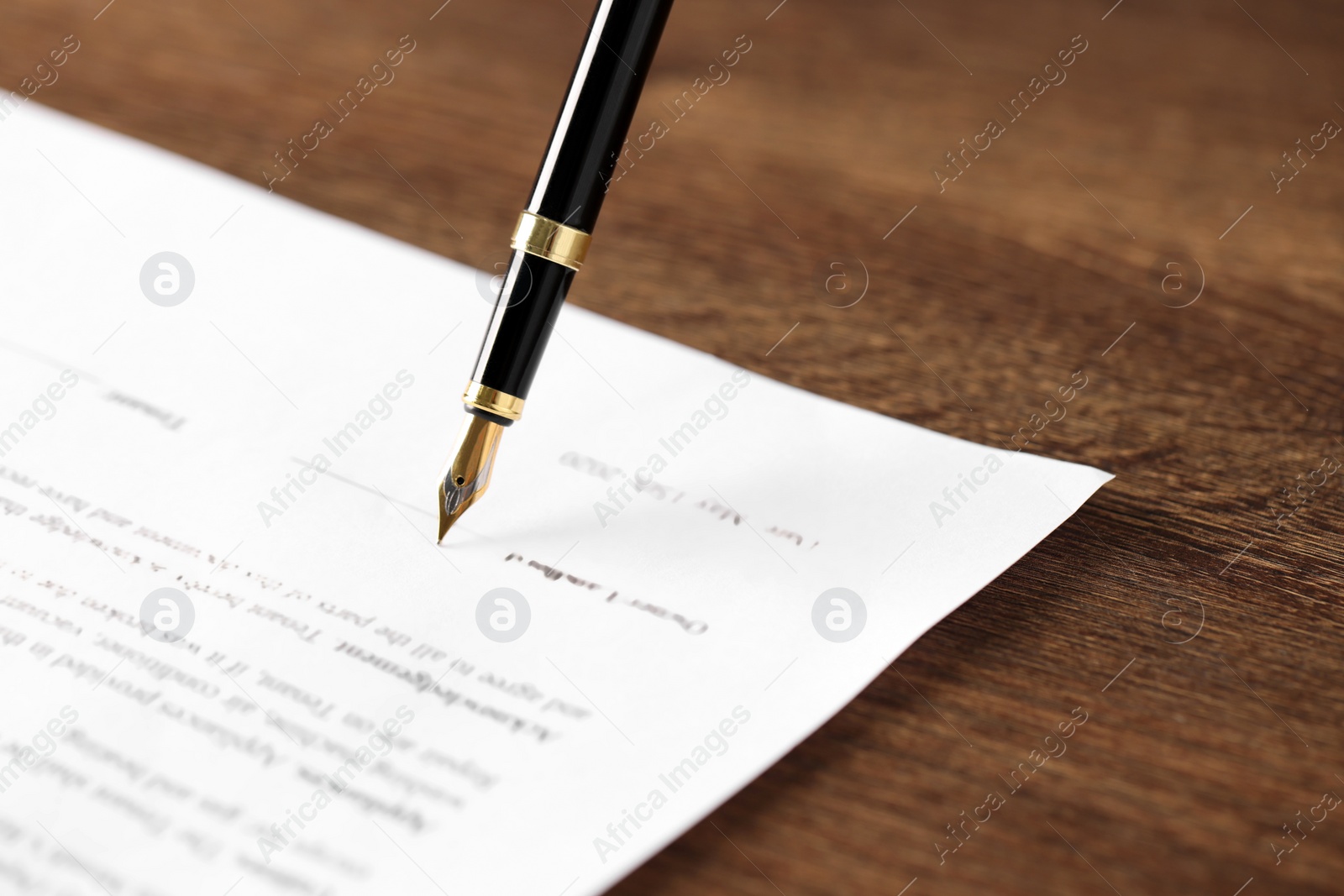 Photo of Writing on document with fountain pen at wooden table, closeup. Notary contract