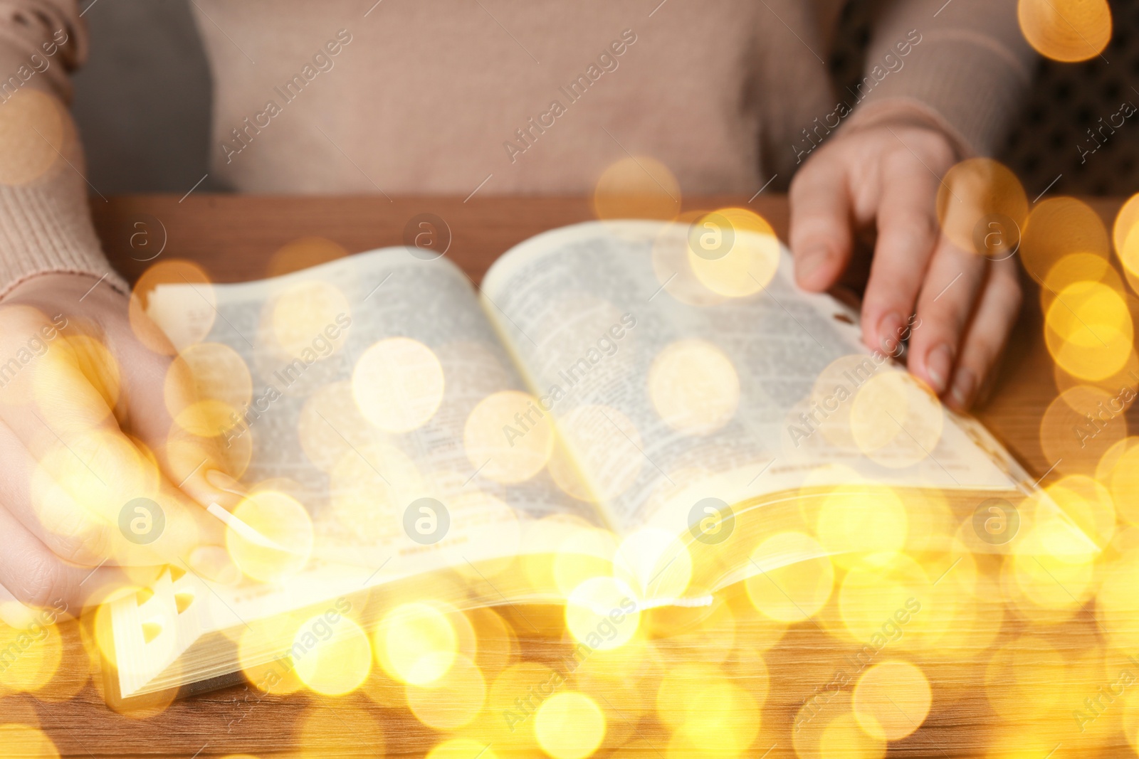 Image of Woman reading Bible at wooden table, closeup. Bokeh effect