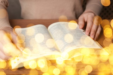 Image of Woman reading Bible at wooden table, closeup. Bokeh effect