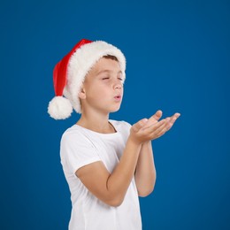 Happy little child in Santa hat on blue background. Christmas celebration