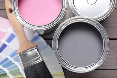 Cans of pink and grey paints, palette with brush on wooden table, flat lay