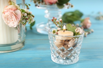 Glass holder with burning candle and floral decor on light blue wooden table, closeup