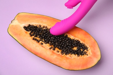 Photo of Half of papaya and vibrator on violet background, top view. Sex concept