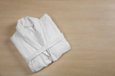 Photo of Clean folded bathrobe on wooden background, top view. Space for text