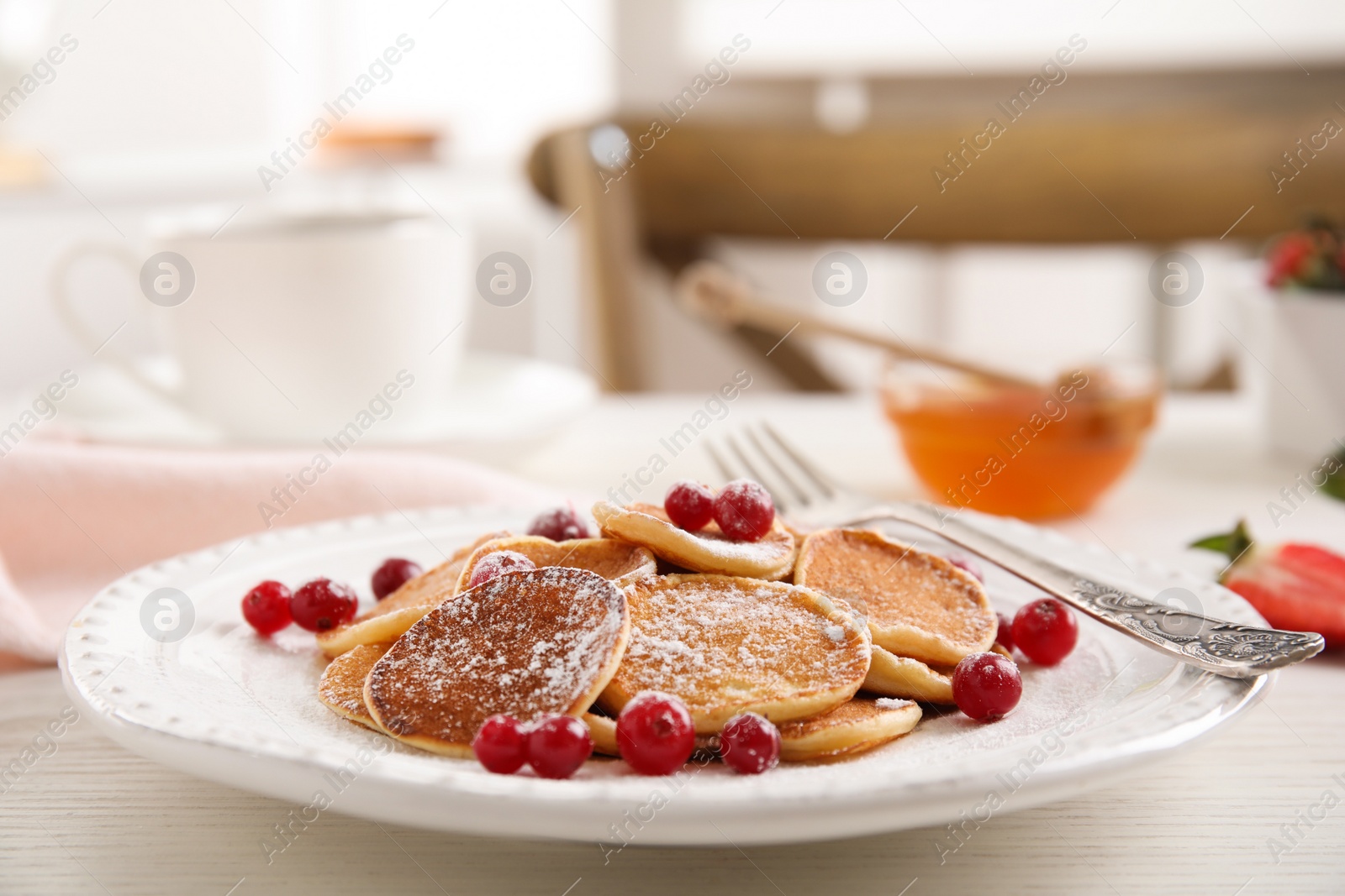 Photo of Delicious mini pancakes cereal with cranberries served on white wooden table