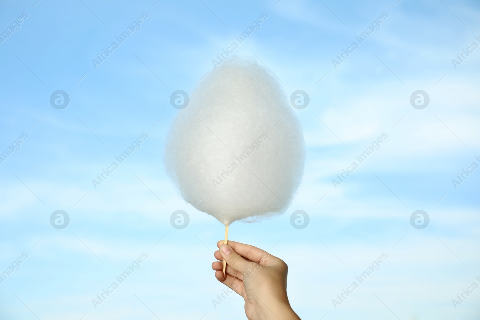 Photo of Woman holding sweet cotton candy on blue sky background, closeup view