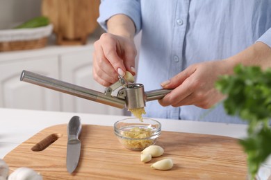 Photo of Woman squeezing garlic with press at wooden table in kitchen, closeup
