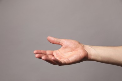 Man holding something in hand on grey background, closeup. Space for text