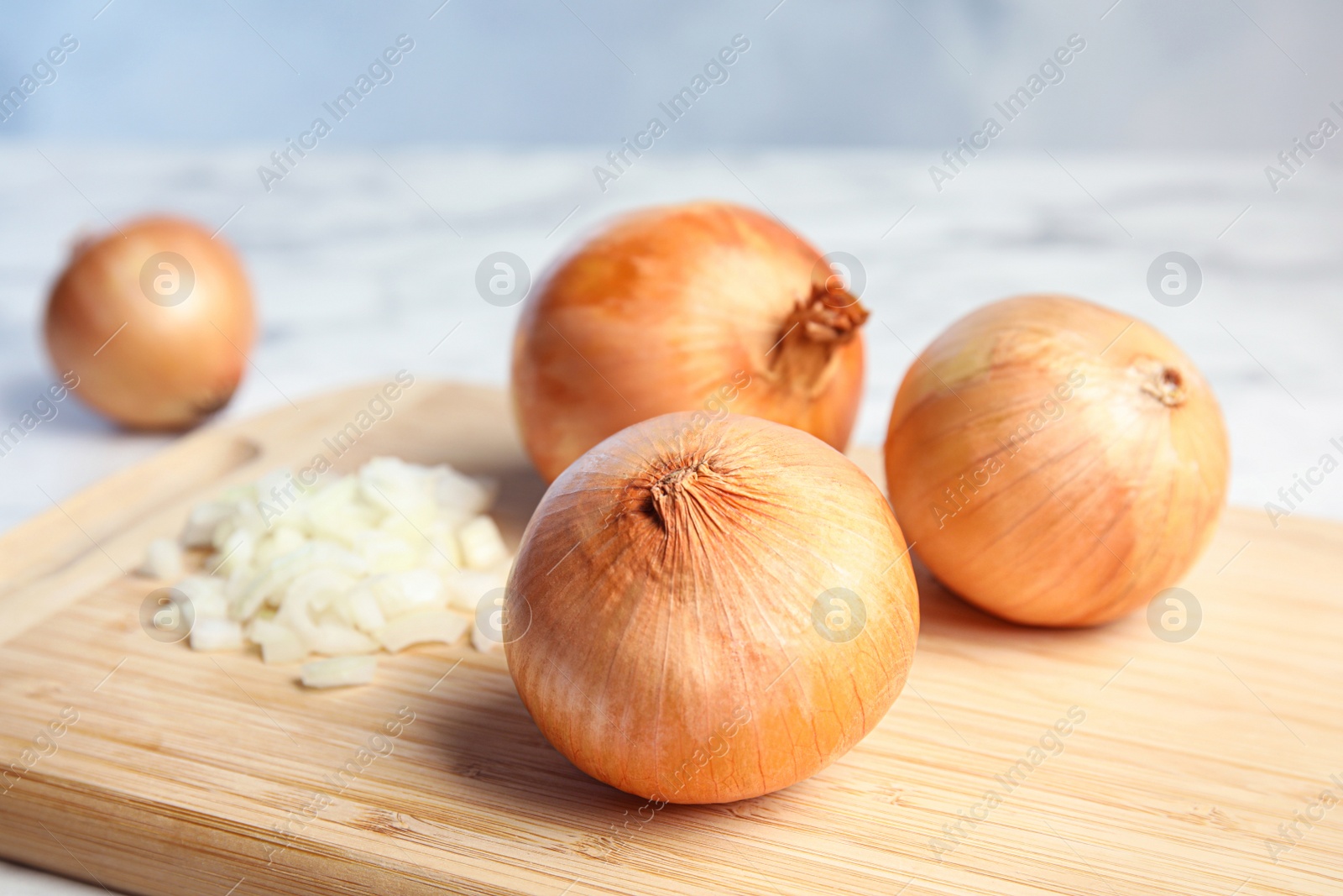 Photo of Wooden board with chopped and whole onions on table, space for text