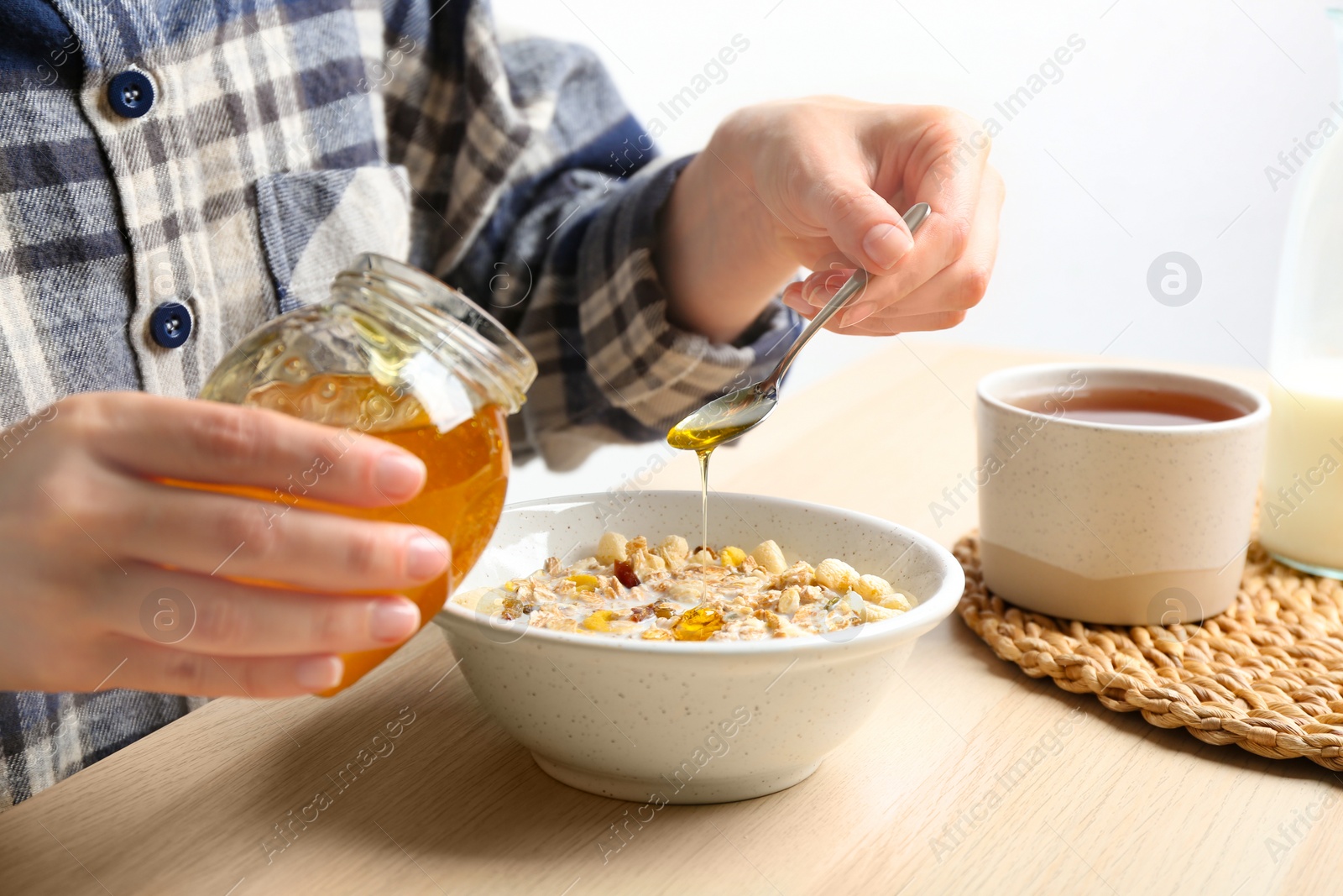 Photo of Woman putting honey into bowl with muesli at wooden table, closeup