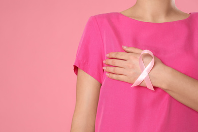 Closeup view of woman with pink ribbon on color background, space for text. Breast cancer awareness