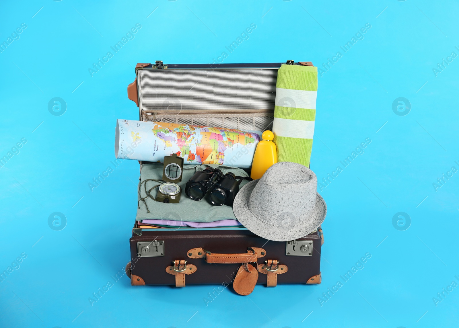 Photo of Open vintage suitcase with clothes packed for summer vacation on light blue background