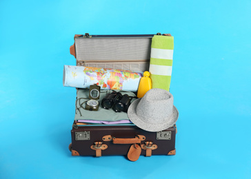 Photo of Open vintage suitcase with clothes packed for summer vacation on light blue background