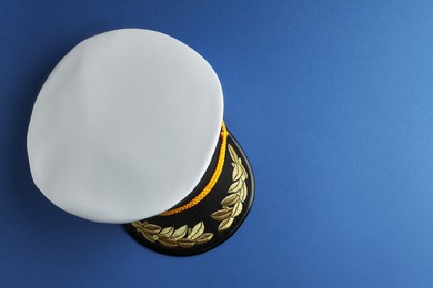 Peaked cap with accessories on blue background, top view. Space for text