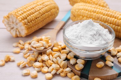 Photo of Bowl with corn starch, ripe cobs and kernels on wooden table