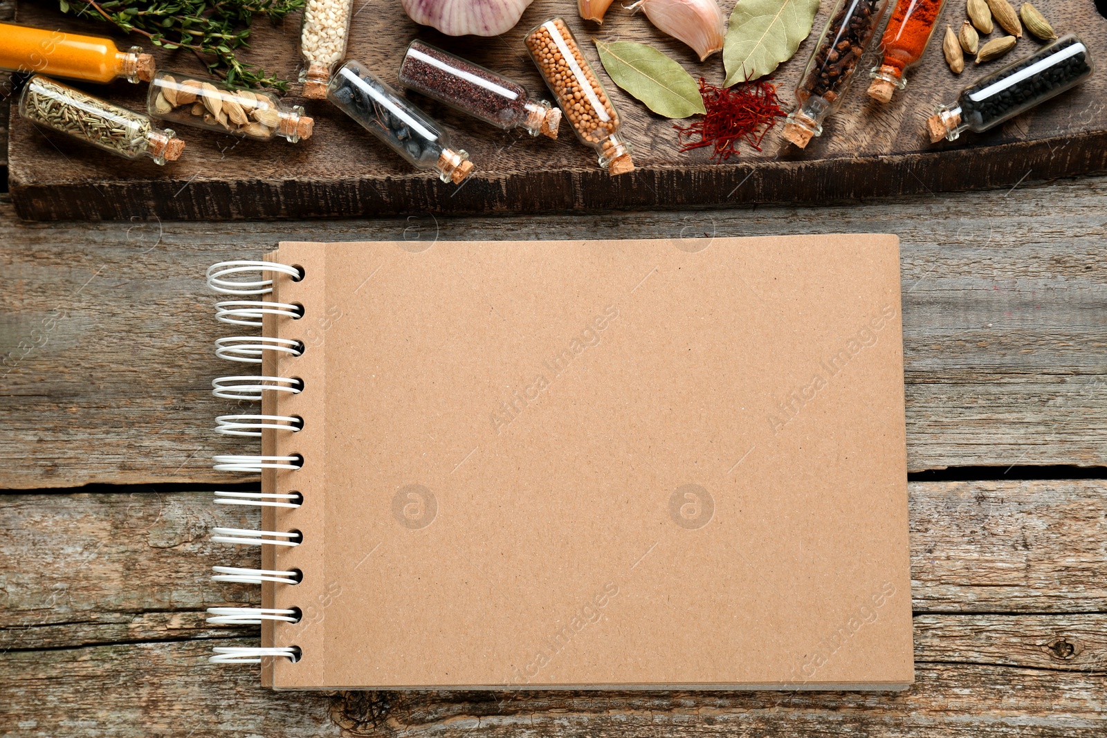 Photo of Blank recipe book and bottles with different spices on old wooden table, flat lay. Space for text