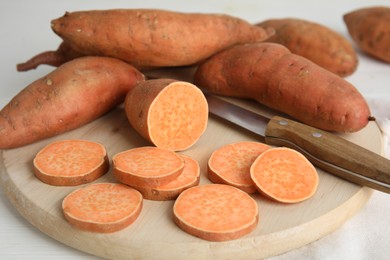 Photo of Whole and cut ripe sweet potatoes on white wooden table