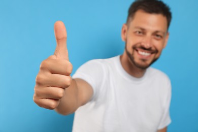 Photo of Man showing thumb up against light blue background, focus on hand. Space for text