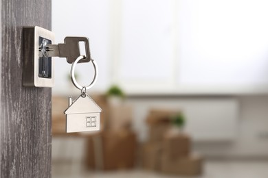 Photo of Mortgage and real estate. Open door with key and house shaped keychain against blurred background, space for text