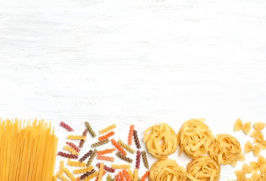 Beautiful composition with different raw pasta on wooden background, top view