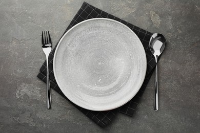 Photo of Empty plate, cutlery and checkered napkin on grey textured table, top view