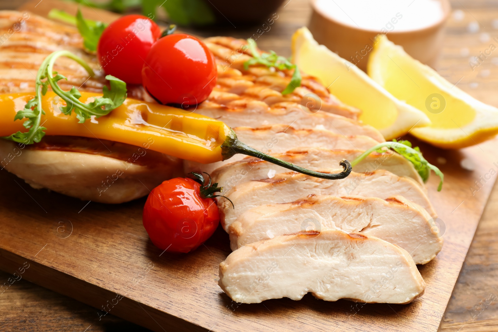 Photo of Tasty grilled chicken fillets with tomatoes and chili pepper on wooden table, closeup
