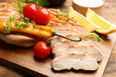 Tasty grilled chicken fillets with tomatoes and chili pepper on wooden table, closeup