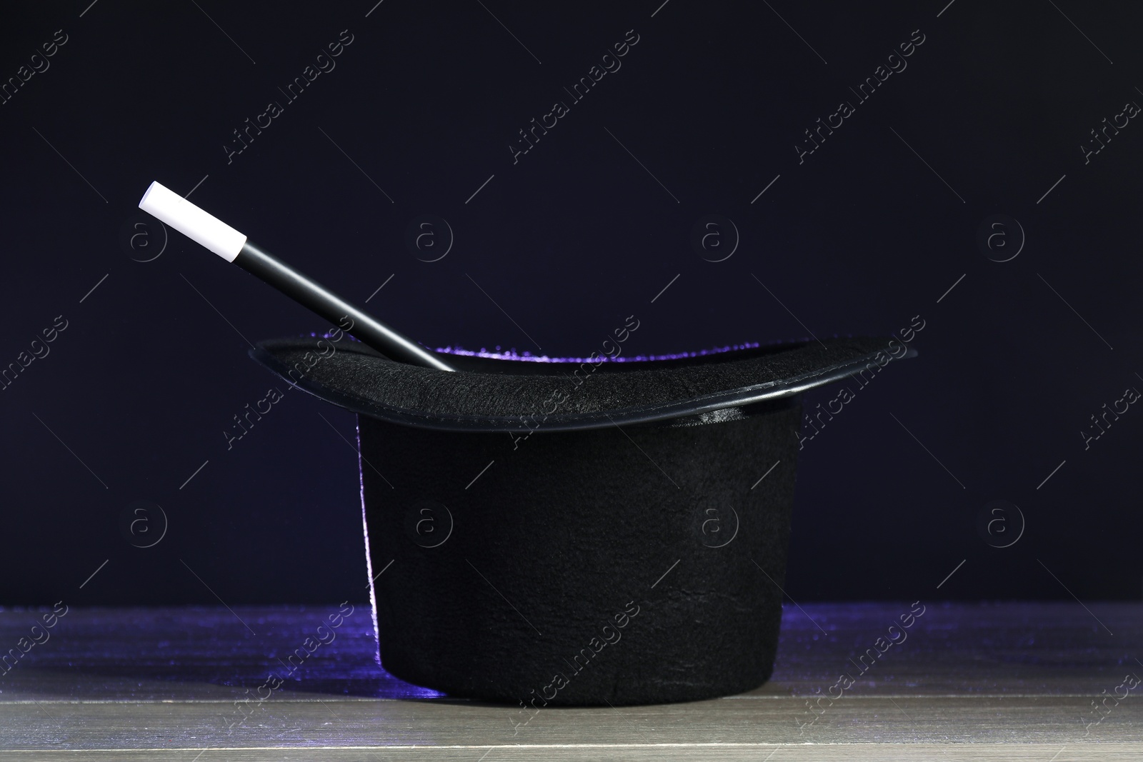 Photo of Magician's hat and wand on wooden table against black background