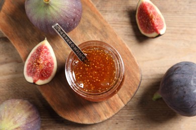 Glass jar with tasty sweet jam and fresh figs on wooden table, flat lay