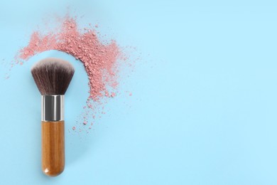 Makeup brush and scattered blush on light blue background, top view. Space for text