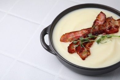 Photo of Delicious potato soup with bacon and microgreens in bowl on white tiled table, closeup. Space for text