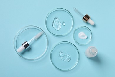 Petri dishes with samples of cosmetic serums, bottle and pipettes on light blue background, flat lay