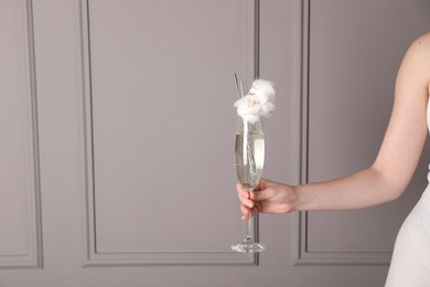 Woman holding glass of cotton candy cocktail near grey wall, closeup. Space for text