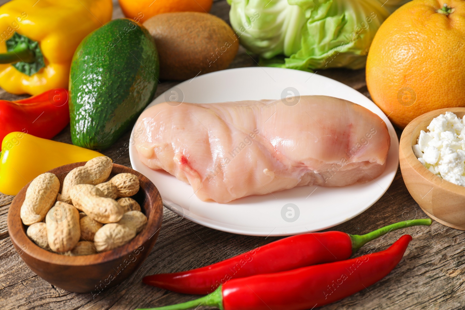 Photo of Healthy meal. Different vegetables and raw chicken breast on wooden table, closeup