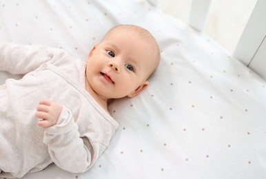 Photo of Cute little baby lying in crib at home, top view