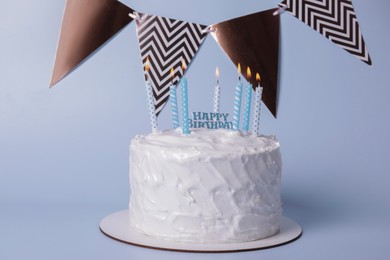 Photo of Delicious cake with cream and burning candles on light blue background