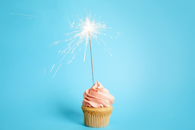 Photo of Birthday cupcake with sparkler on light blue background