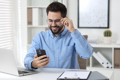 Photo of Happy young man using smartphone at white table in office